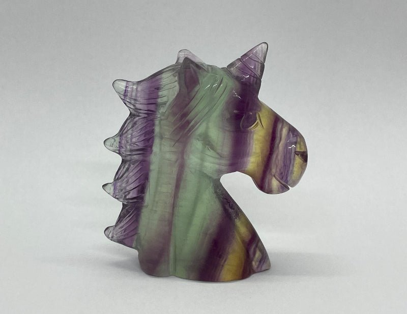 Handgefertigtes Einhorn aus Regenbogen-Fluorit mit violett-grüner Maserung, seitliche Ansicht.